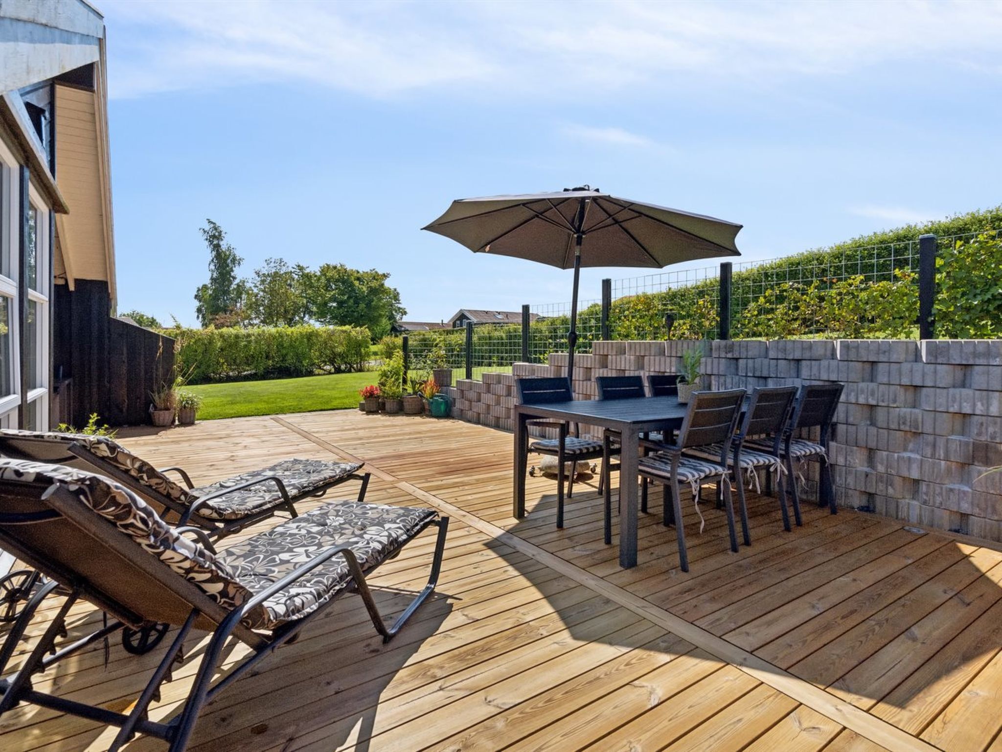 Een terras buiten met een houten terras, een tafel met stoelen en een grote parasol.