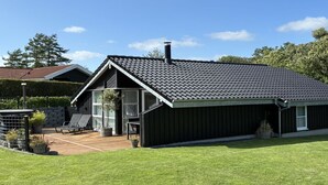 A modern two-story house with a sloped roof, a covered patio with outdoor furniture, and a well-maintained lawn.
