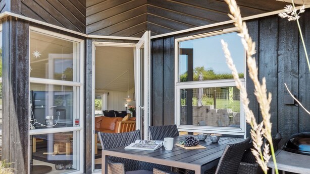 A wooden deck with a dining table and chairs, large sliding glass doors leading to an interior space with a sofa and a dining table.