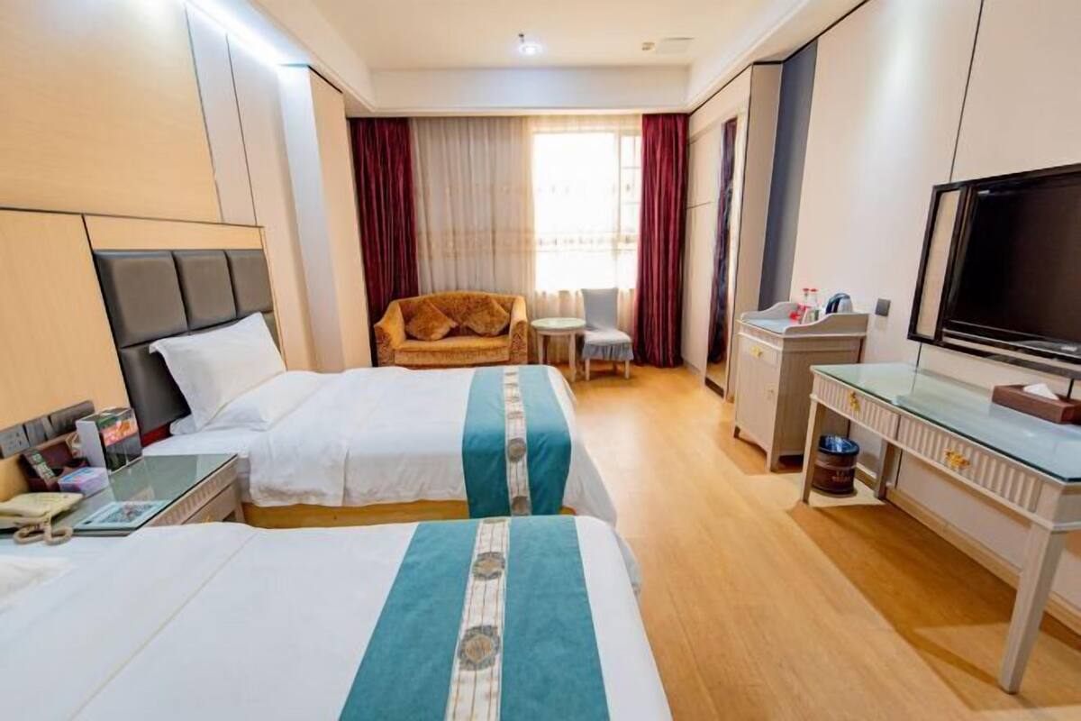 Ein Hotelzimmer mit zwei Betten, einem Schlafsofa, einem Fernseher, einem Schreibtisch und einem kleinen Tisch.
