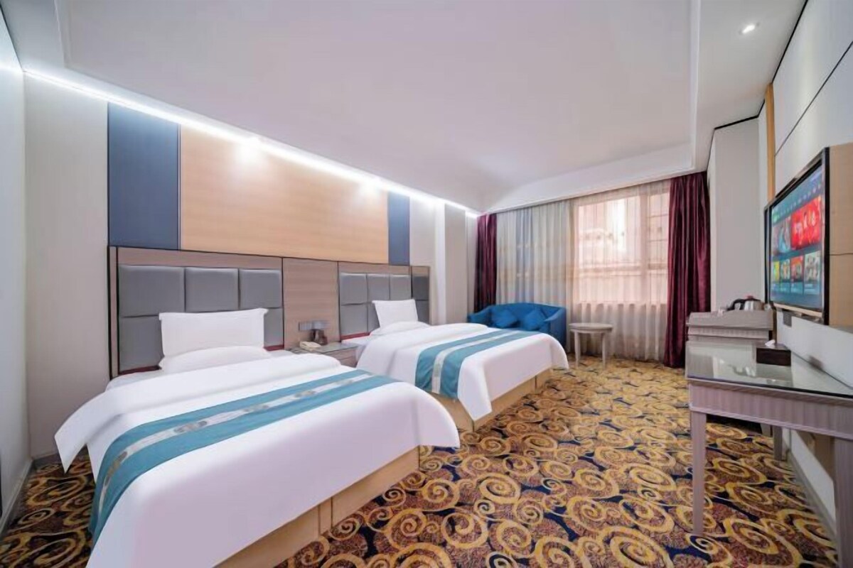 Ein Hotelzimmer mit zwei Betten, einem Schreibtisch, einem Stuhl, einem Fernseher und einem gemusterten Teppich.