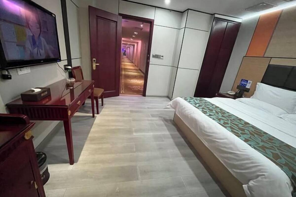 Ein Hotelzimmer mit Bett, Schreibtisch, Fernseher und einem Gang zu weiteren Zimmern.