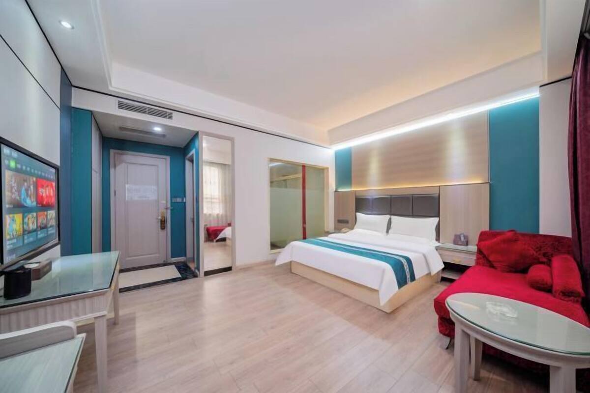 Ein Hotelzimmer mit einem Bett, einem Fernseher, einem roten Sofa und einem Glastisch.