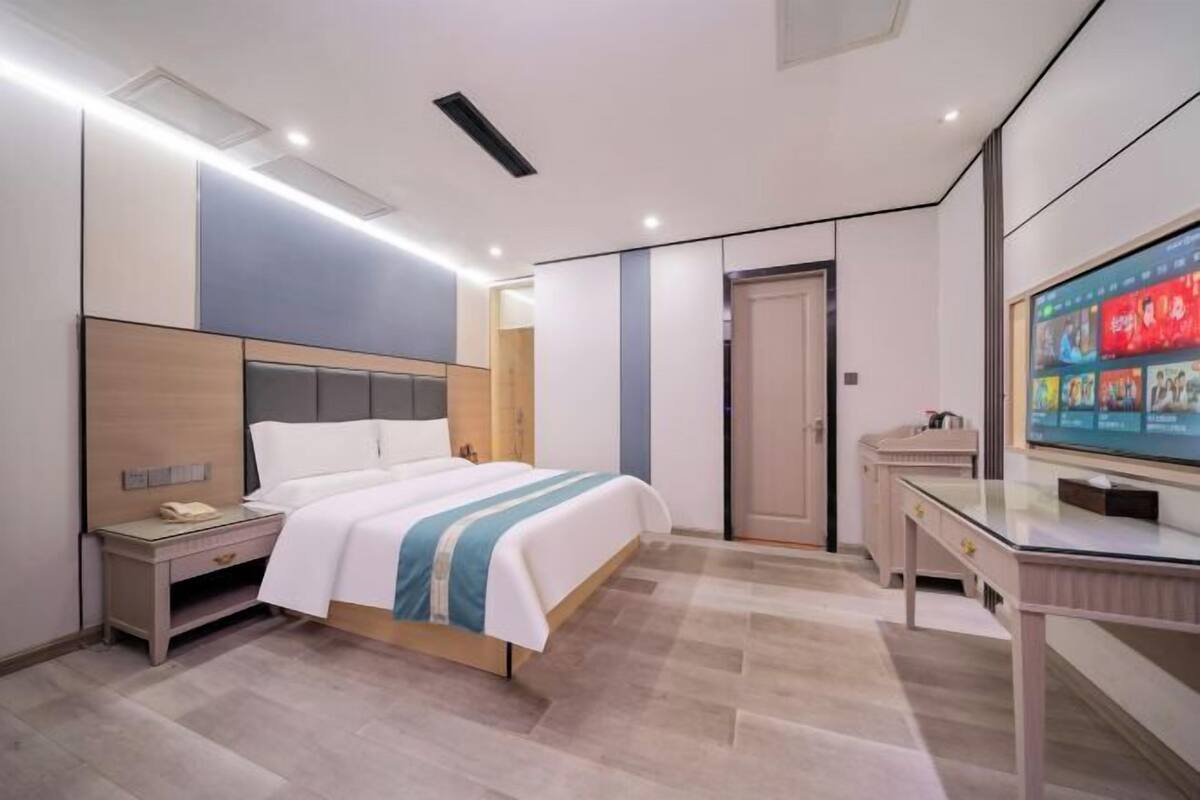 Ein modernes Hotelzimmer mit Bett, Nachttisch, Fernseher und Schreibtisch mit Stuhl.