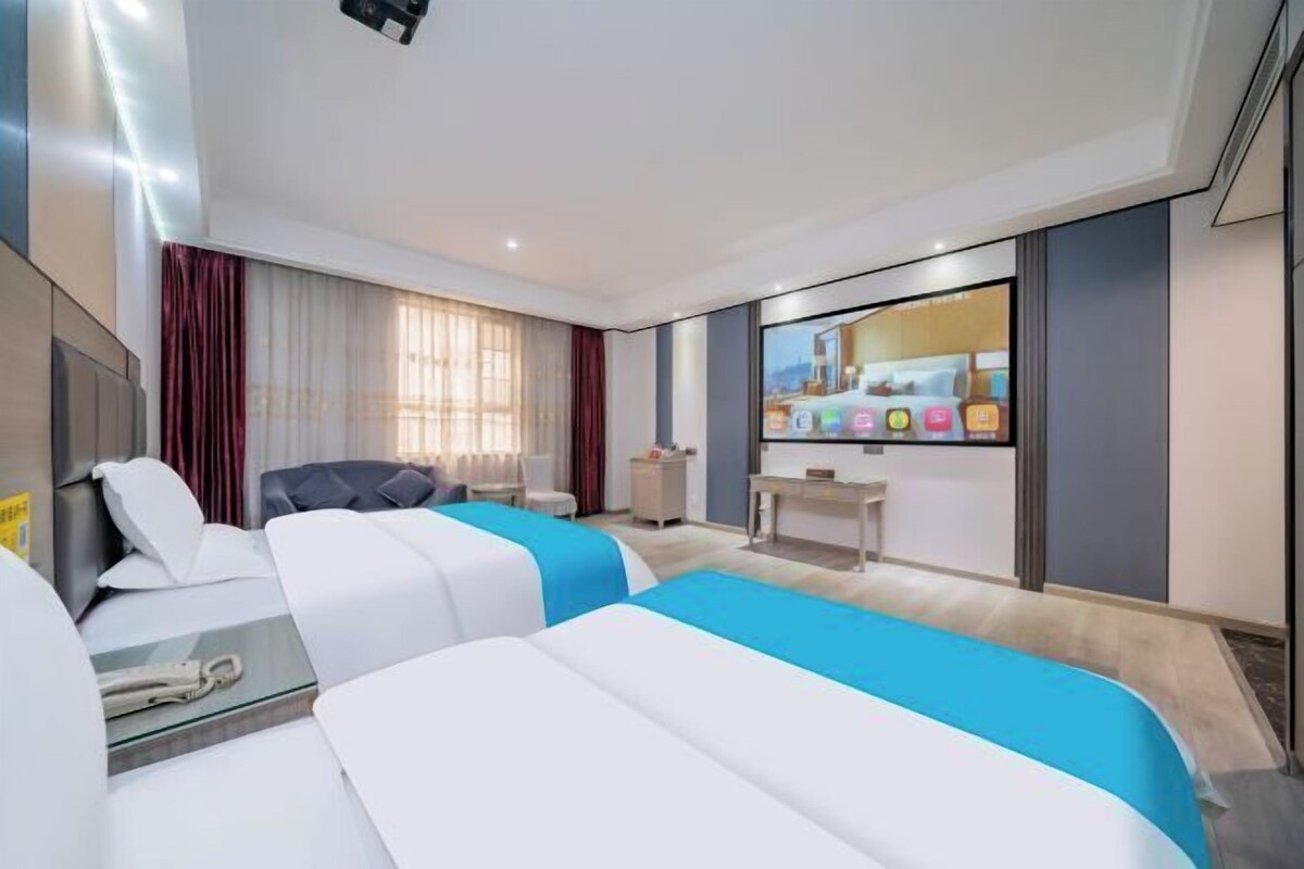 Ein modernes Hotelzimmer mit zwei Betten, einem Schreibtisch, einem Stuhl, einem Fernseher und einem Fenster mit Vorhängen.