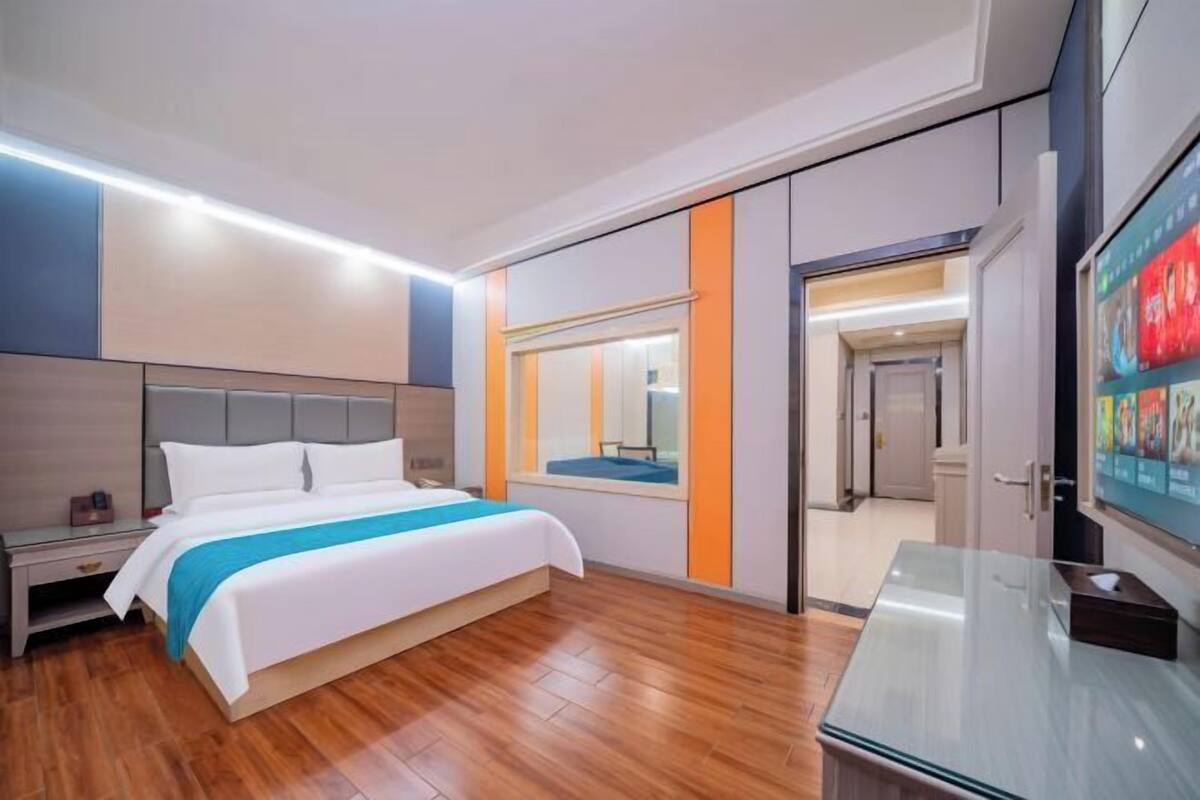 Ein modernes Hotelzimmer mit Bett, Nachttisch und Fernseher auf einem Standfuß.