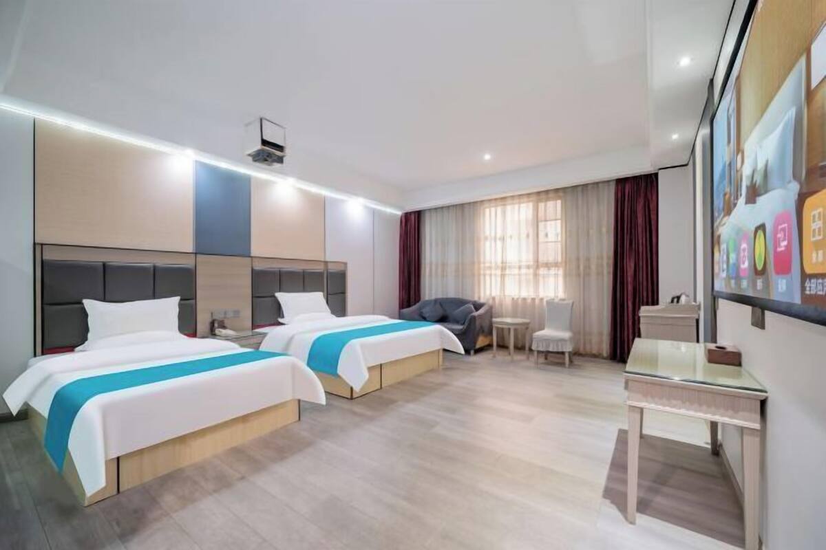 Ein Hotelzimmer mit zwei Betten, einem Schreibtisch, einem Sessel und einem großen Fenster mit Vorhängen.