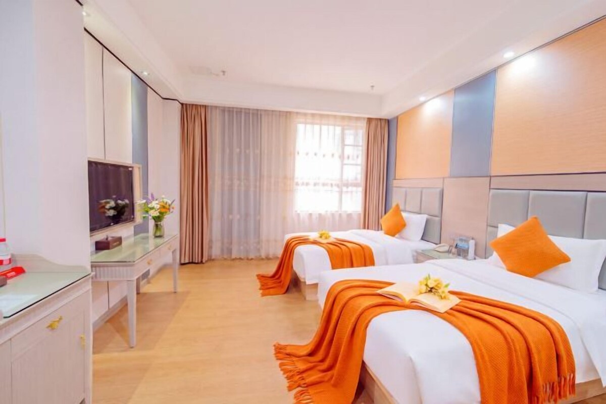 Habitación de hotel con dos camas, un escritorio, un televisor y una ventana con cortinas.