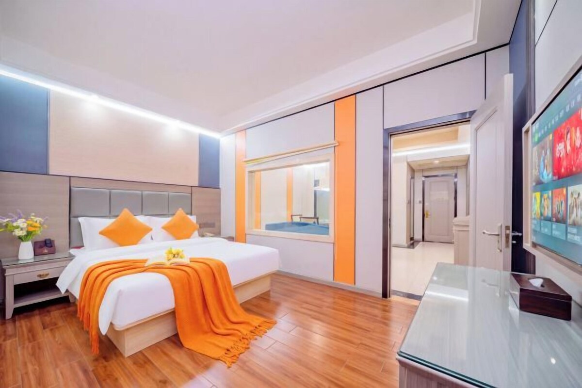 Una habitación de hotel moderna con una cama grande, mesitas de noche, un armario de vidrio y vistas al pasillo.