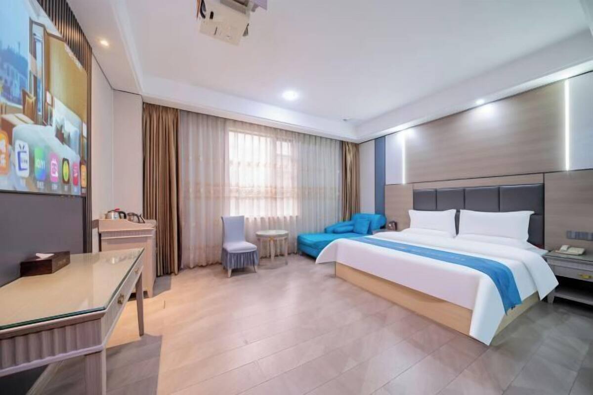 Ein modernes Hotelzimmer mit Bett, Schreibtisch, Stuhl, kleinem Tisch und Fernseher.