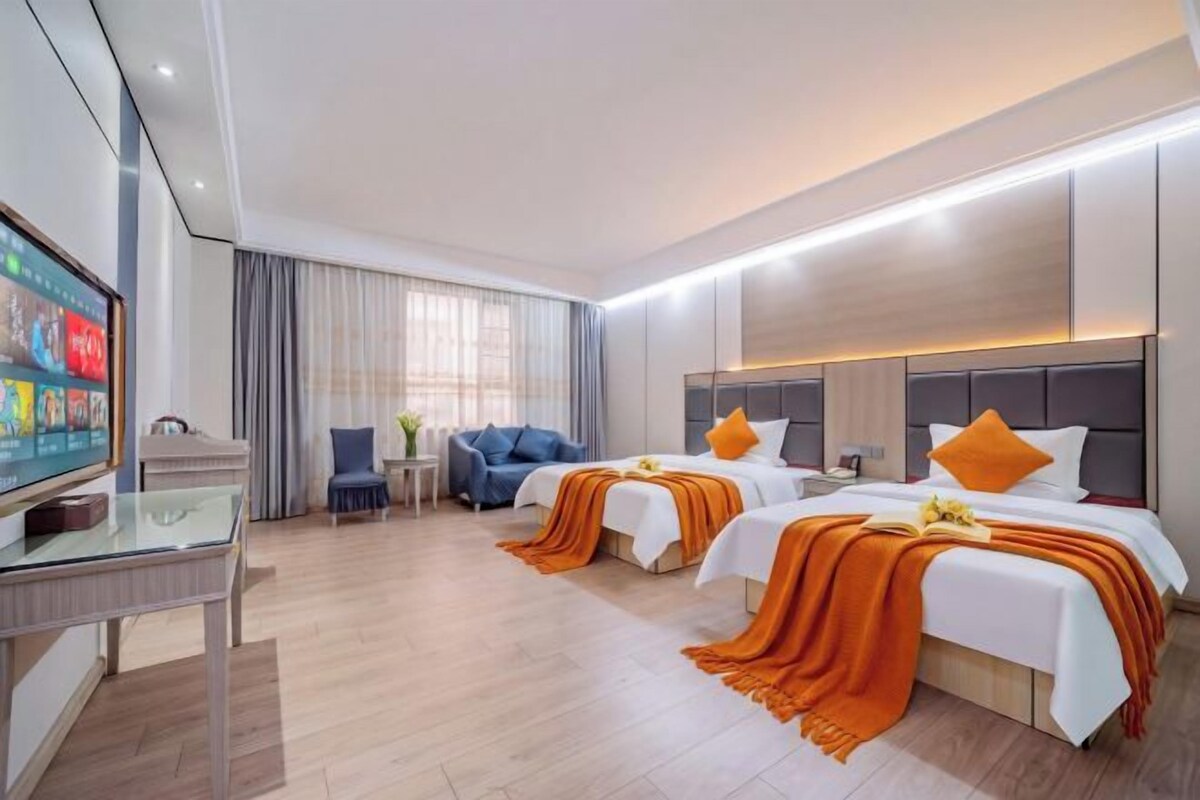 Habitación de hotel con dos camas, televisión, escritorio y ventana con cortinas.