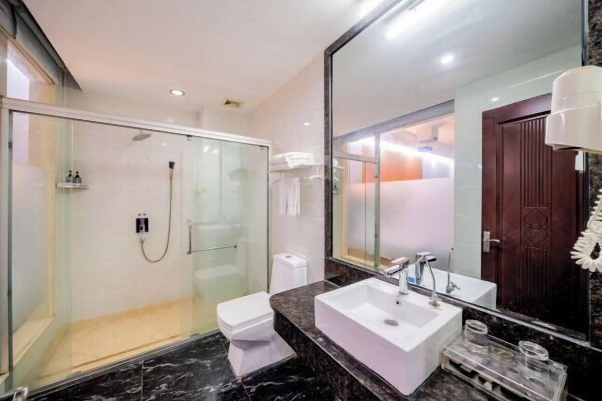 Ein modernes Badezimmer mit einer Glaskabine zur Dusche, einem weißen Waschbecken und einem großen Spiegel.