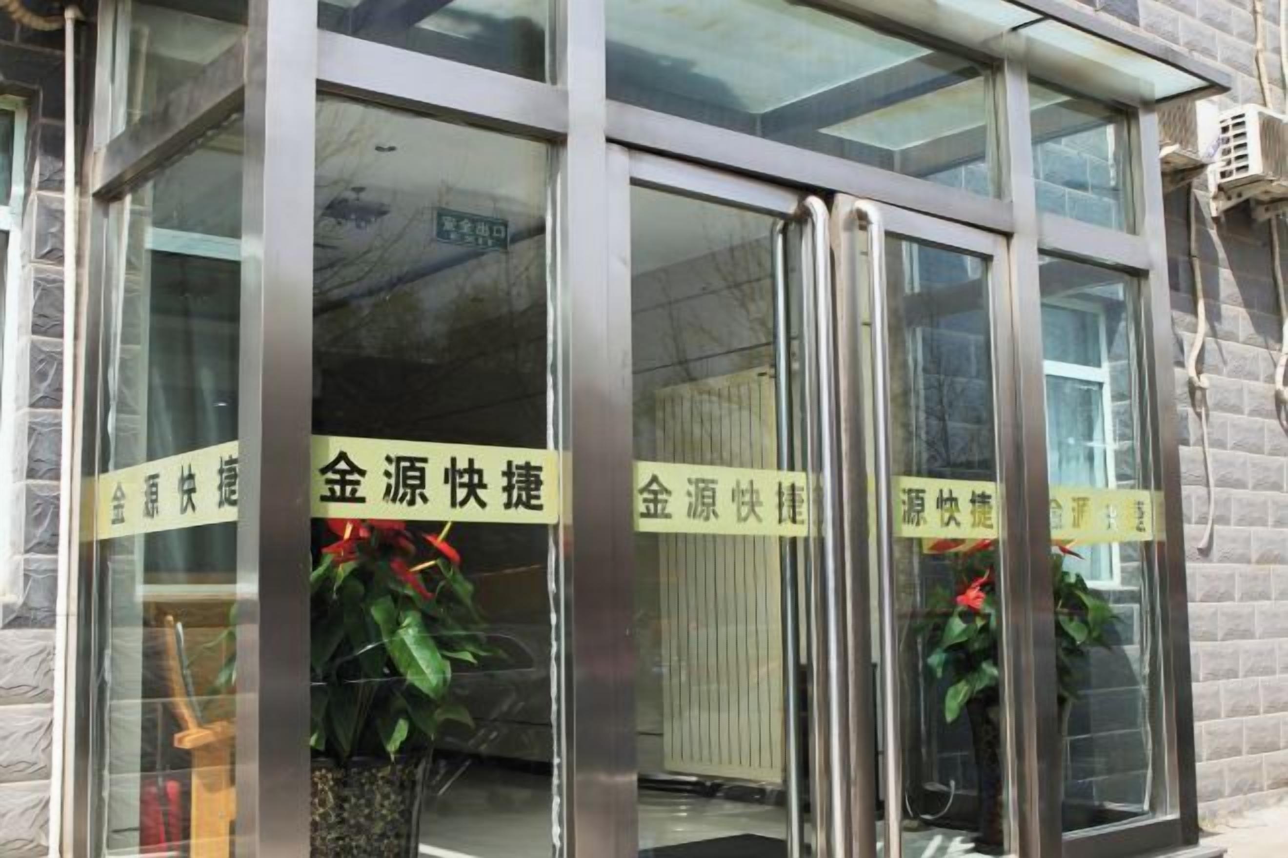 Entrada de edifício com portas de vidro e molduras de metal, com placas contendo caracteres chineses.