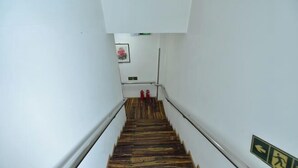 A narrow staircase with wooden steps and white walls, leading to a landing with a framed picture and a fire extinguisher. - Jinyuan Express Hotel (Beijing)