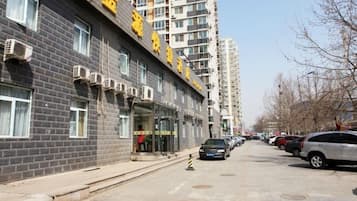 A multi-story building with a visible entrance and parked cars along the street.
