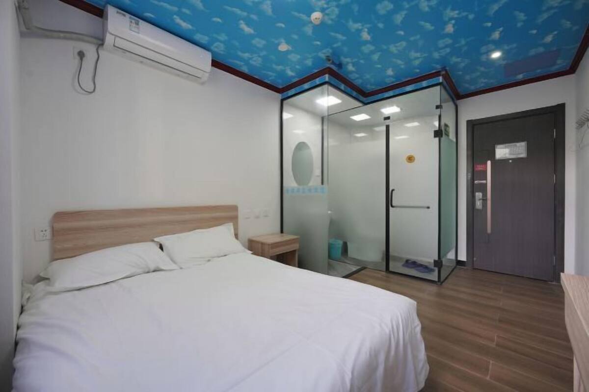 A bedroom with a bed, a glass-enclosed shower, and a door to the bathroom.