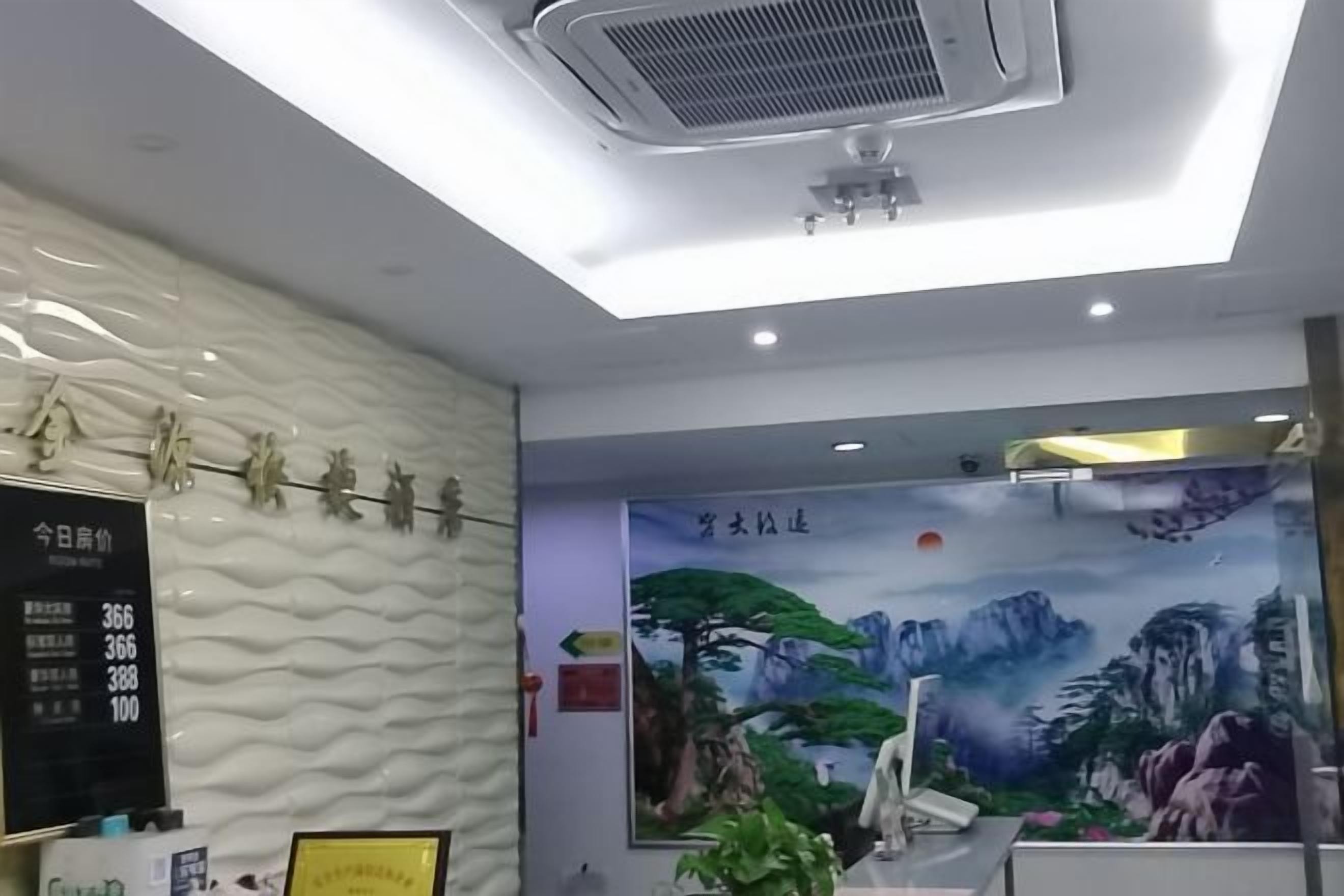 A hotel reception area with a modern design, including a digital display board, a mural of mountains, and a ceiling fan.