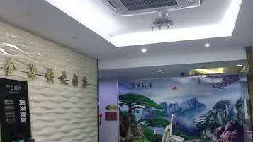 A hotel reception area with a modern design, including a digital display board, a mural of mountains, and a ceiling fan.
