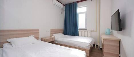 Quarto de hotel com duas camas de solteiro, cabeceira de madeira, mesa de cabeceira pequena, televisão e janela com cortinas.