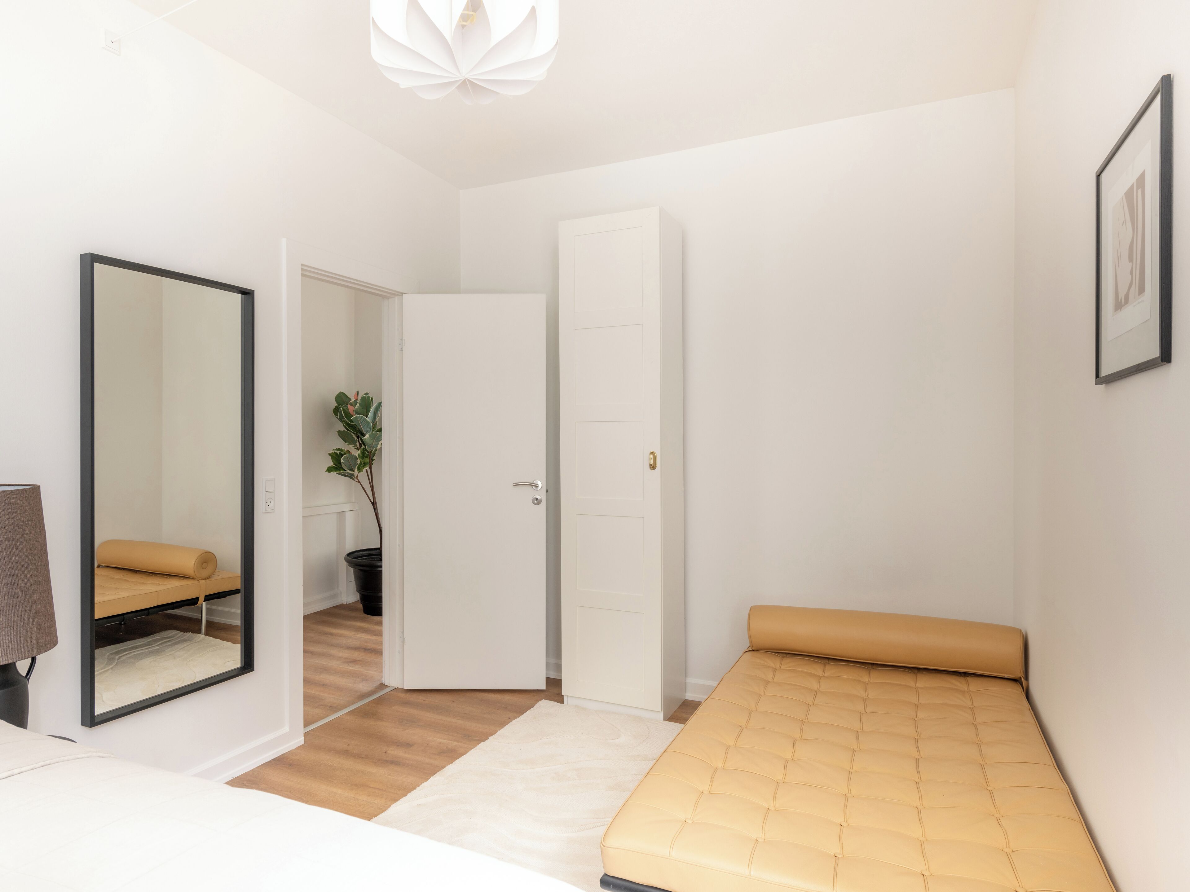 A bedroom with a bed, a mirror, a door, and a potted plant.
