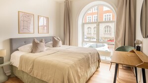A bedroom with a large bed, a desk, a chair, a lamp, and a window with a view of buildings. - Noble - Fantastic 5-Bdr Apt in the Capital (København)