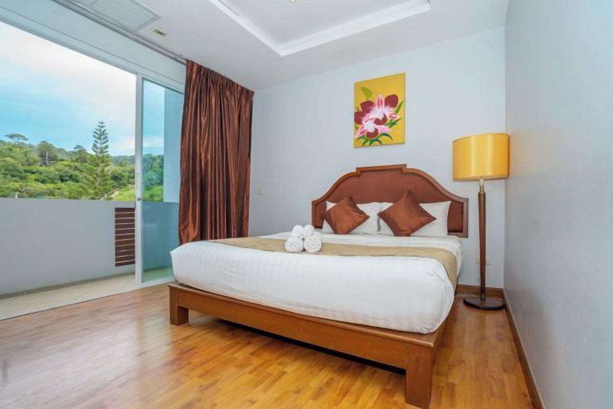 A bedroom with a large bed, a bedside lamp, a window with curtains, and a painting on the wall.