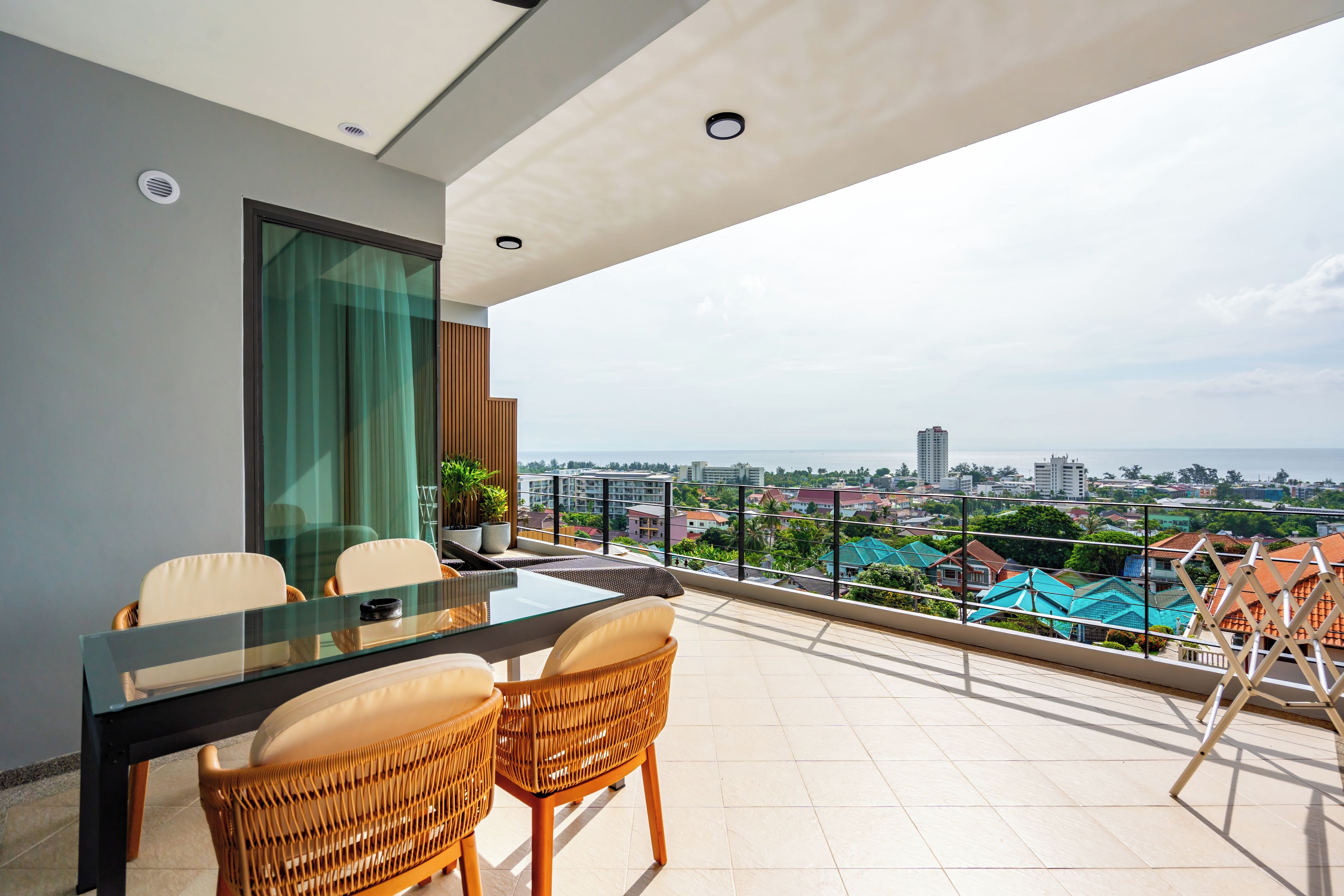 A balcony with a glass table and chairs, a view of a cityscape, and a modern building with a sloped roof.