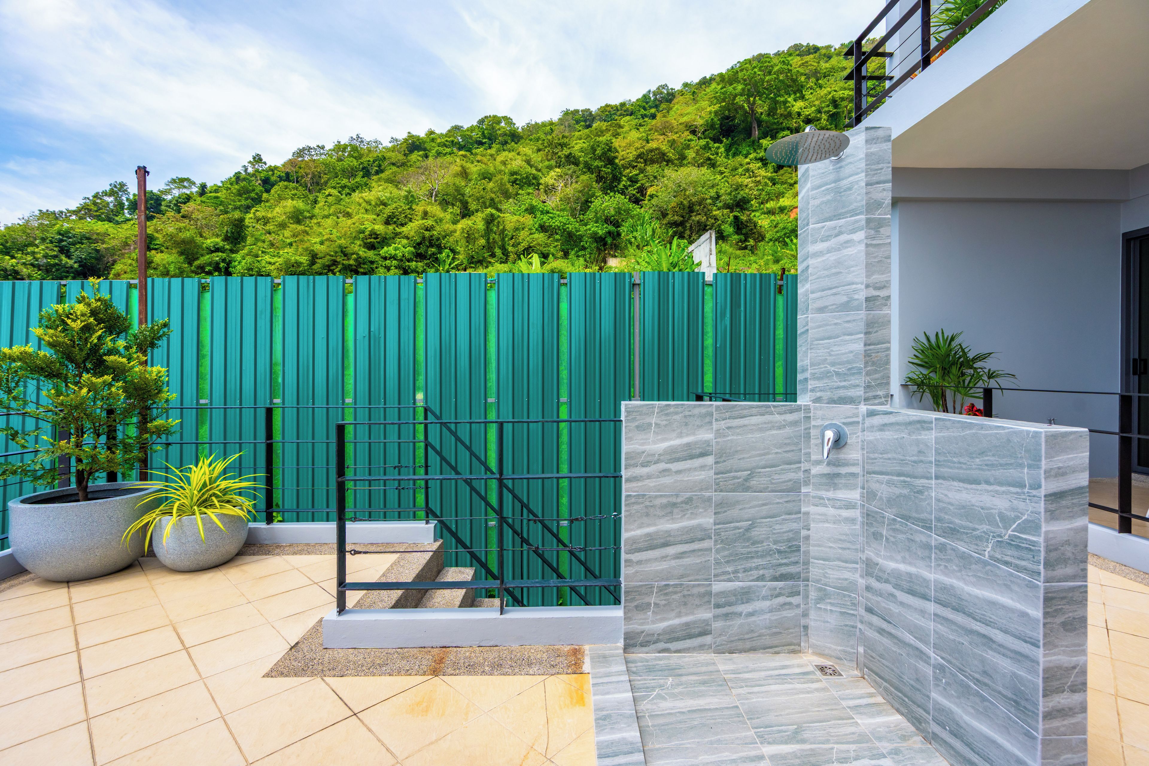 A modern outdoor area with a green fence, potted plants, and a tiled floor.
