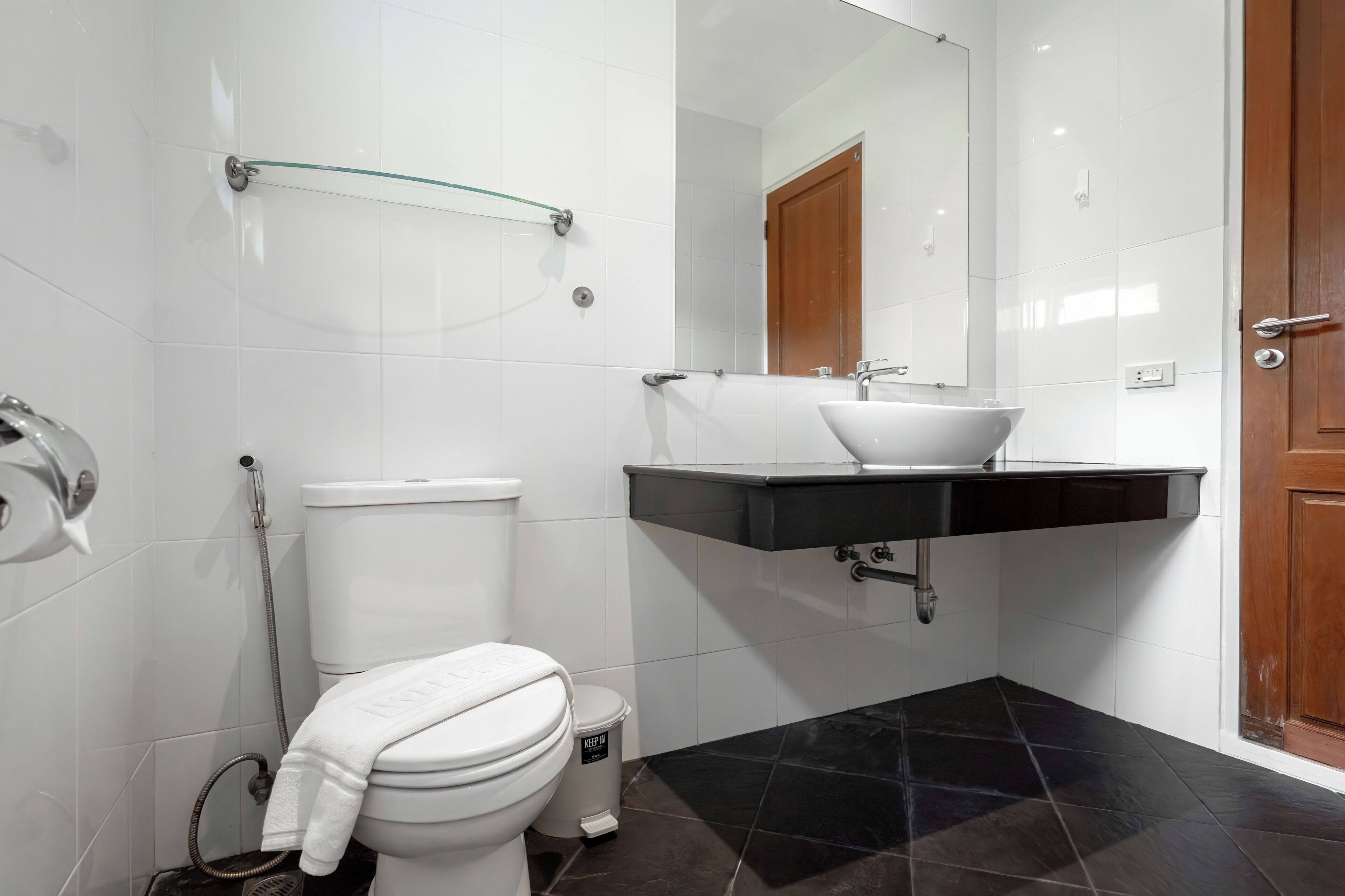 A modern bathroom with white tiles, a black sink, and a glass shelf.