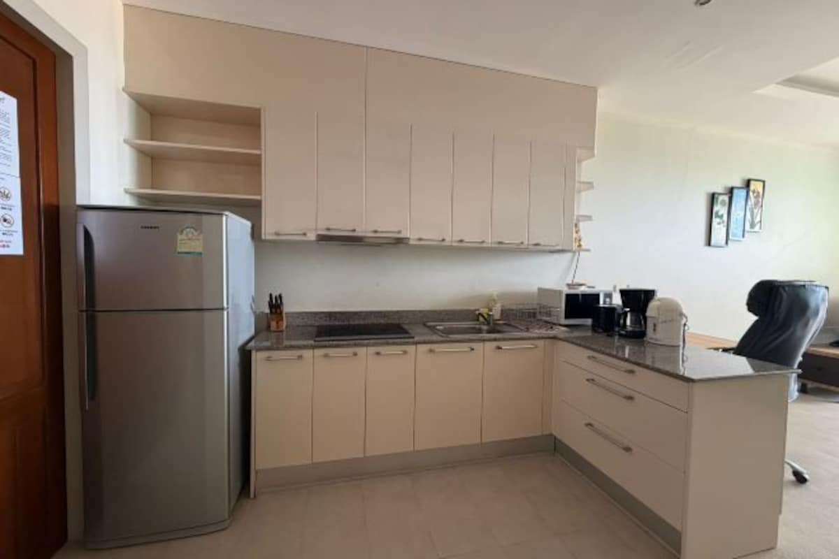 Cocina compacta con refrigerador integrado, pileta y encimera con cafetera.