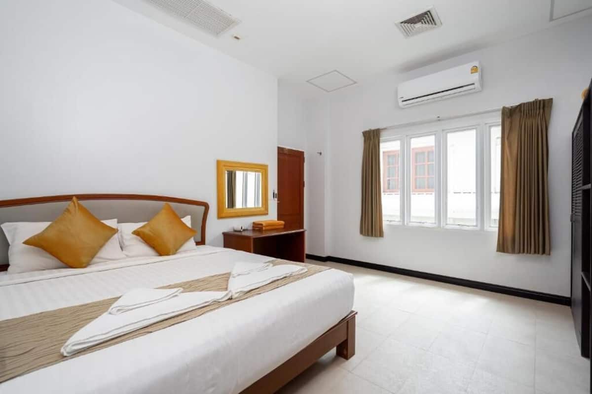 Habitación de hotel con cama, espejo, armario, aire acondicionado y ventana con cortinas.