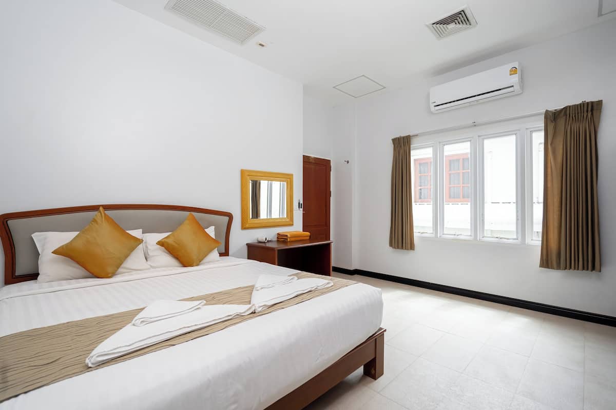 Una habitación de hotel con una cama grande, un cabecero de madera, una mesita de noche, un espejo, un equipo de aire acondicionado y una ventana con cortinas.