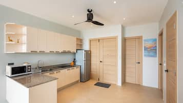 A modern kitchen with a built-in microwave, a sink, and a refrigerator. There are wooden cabinets and a ceiling fan.