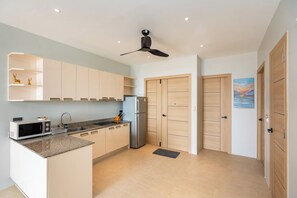 A modern kitchen with a built-in microwave, a sink, and a refrigerator. There are wooden cabinets and a ceiling fan. - Hillside Seaview Residence (Karon)