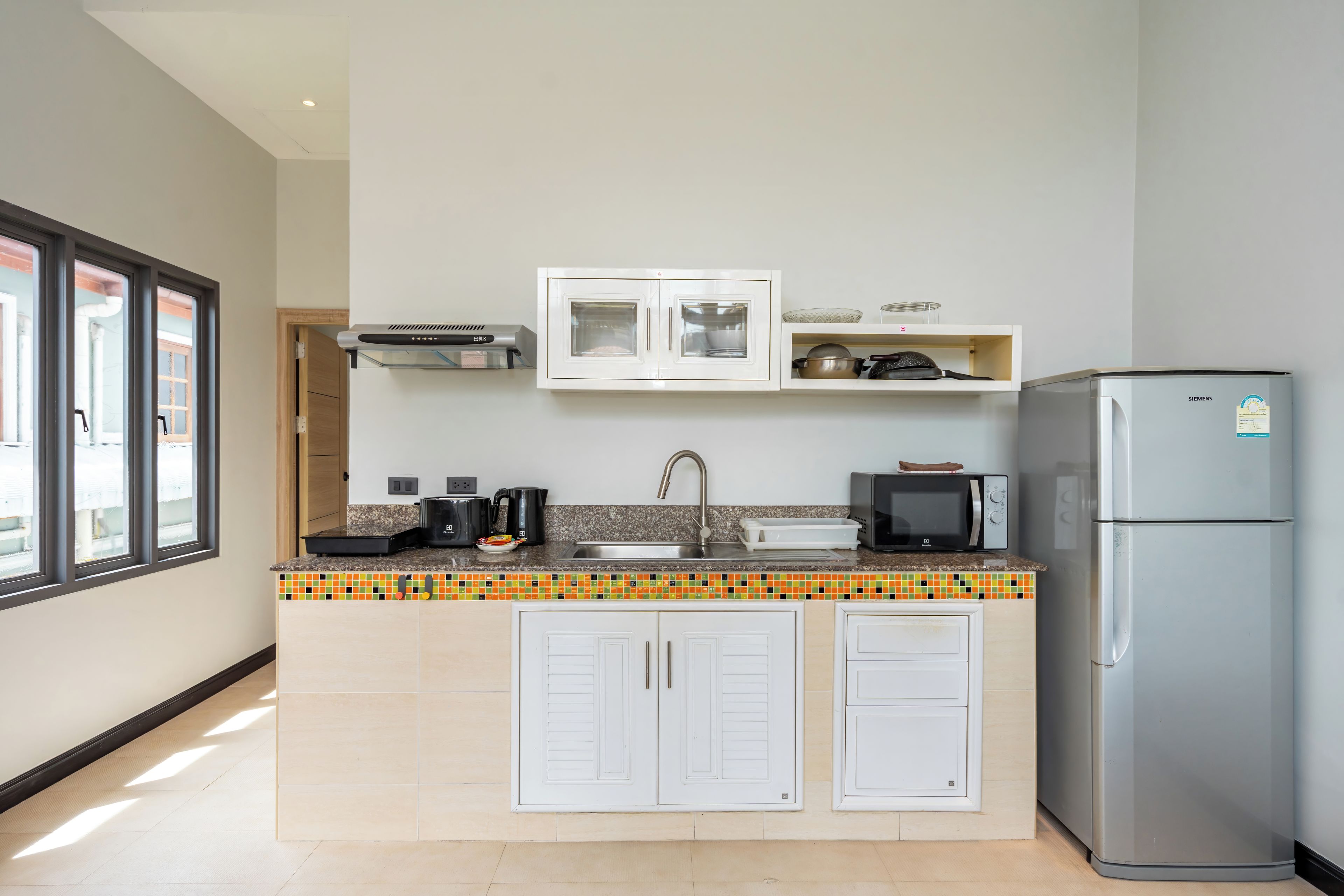 A modern kitchen with white cabinets, a stainless steel refrigerator, a microwave, and a coffee maker.