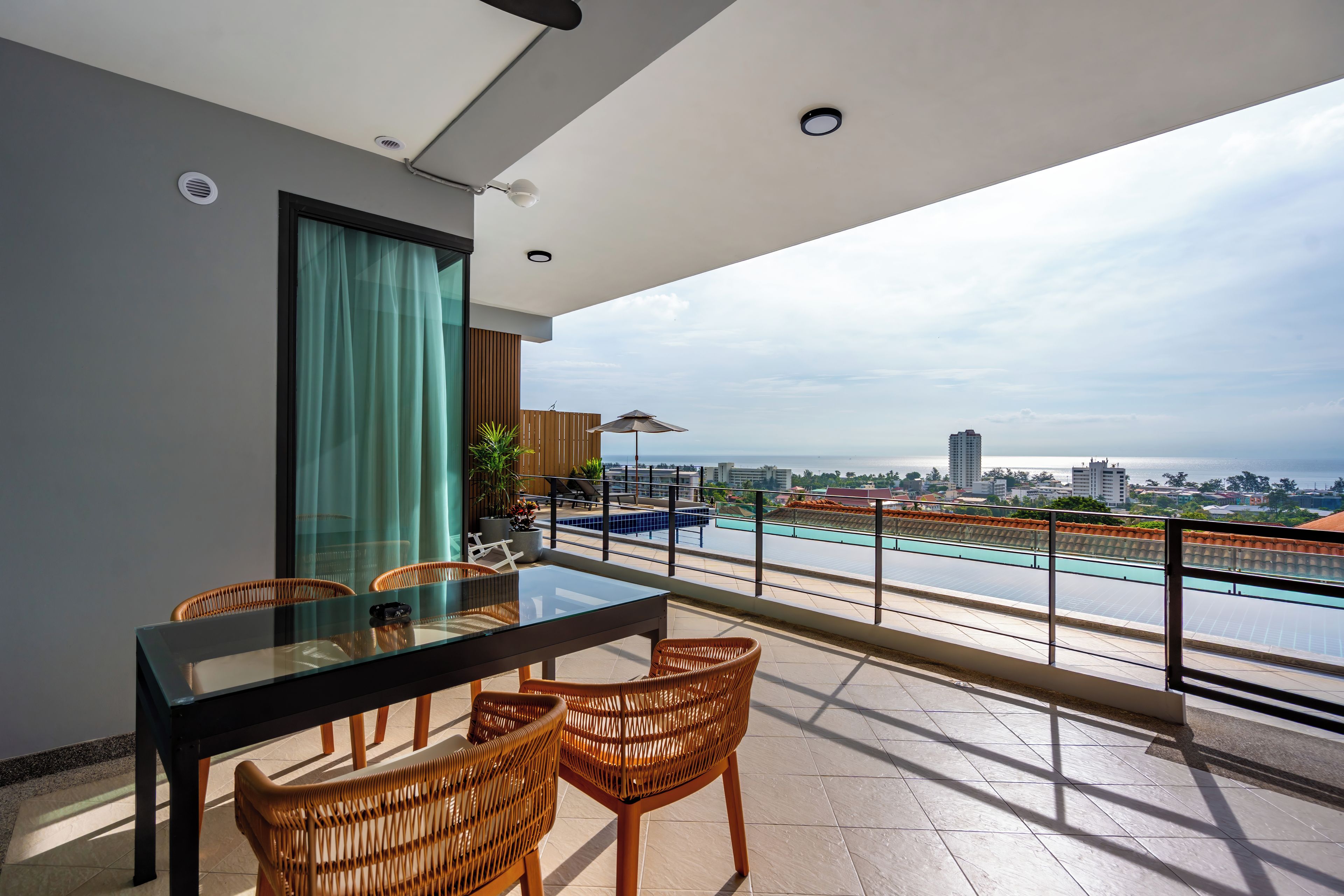 Un balcon avec une table et des chaises en verre, une vue sur une piscine et un paysage urbain en arrière-plan.