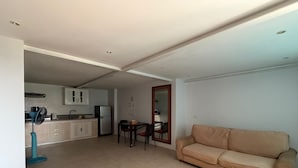 A living room with a beige sofa, a dining table with chairs, a kitchen area with cabinets and appliances, and a large mirror on the wall. - Hillside Seaview Residence (Karon)