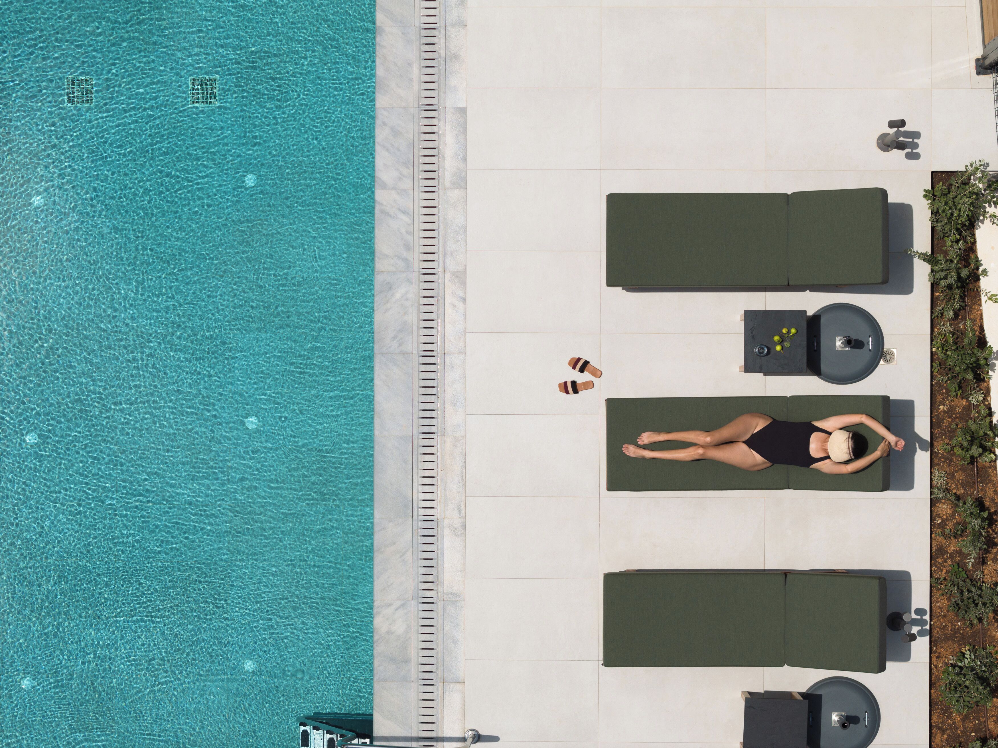 Une vue aérienne d’un espace aménagé autour d’une piscine, avec des chaises longues, une petite table avec des boissons et une personne qui se détend.