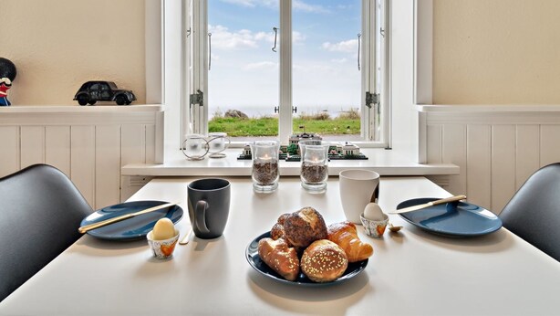A dining table with pastries, a coffee mug, and a view of the sea through a window. - "Malila" - 15m from the sea by Interhome (Hasle)