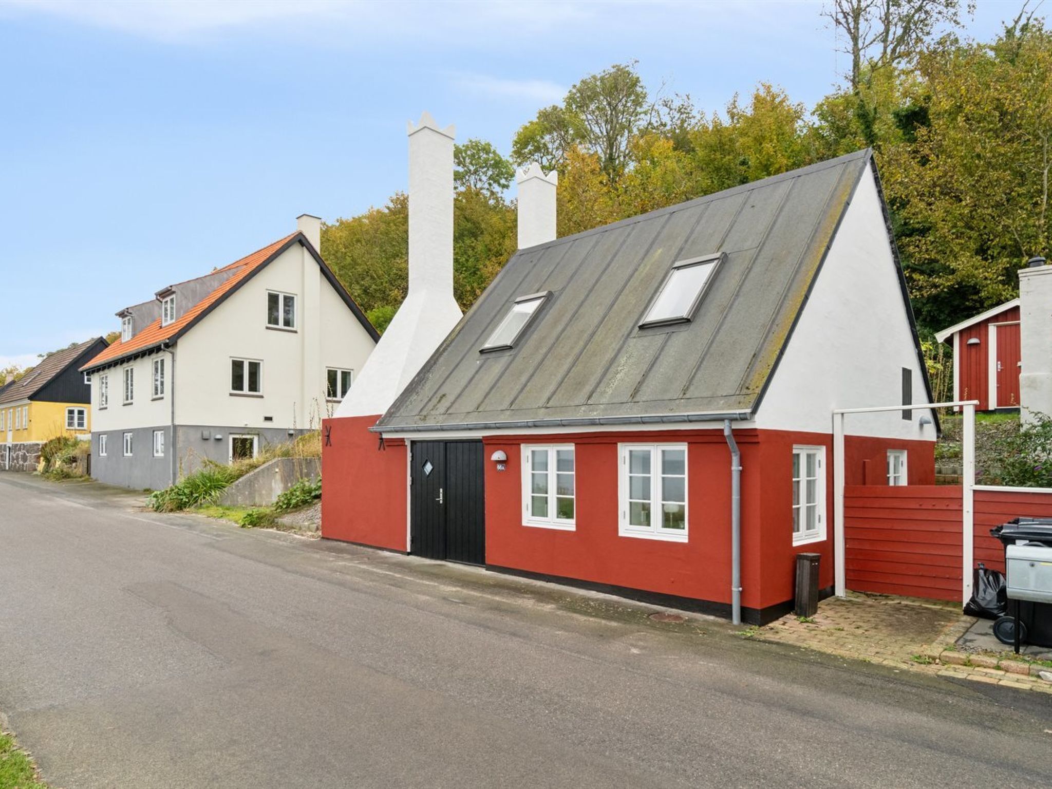 A row of houses with distinct architectural styles, including a red house with a black door and white windows, and a white house with a grey roof.