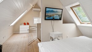 A bedroom with a sloped ceiling, a mounted TV, a bed, a nightstand, and a window with a view of greenery. - "Malila" - 15m from the sea by Interhome (Hasle)
