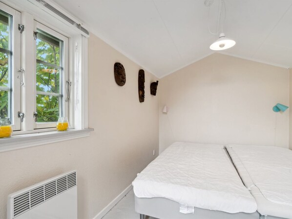 A bedroom with a single bed, a window with a view of trees, and a wall-mounted heater.