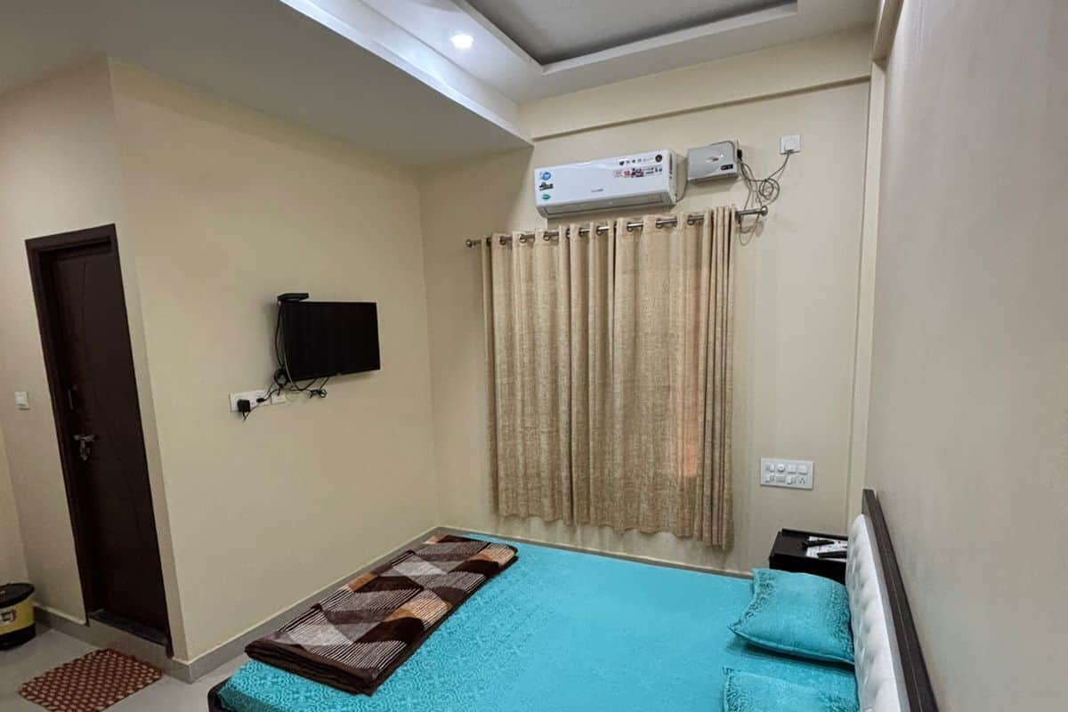 Una camera da letto con un letto, un ventilatore a soffitto, un condizionatore, una TV e una finestra con tende.