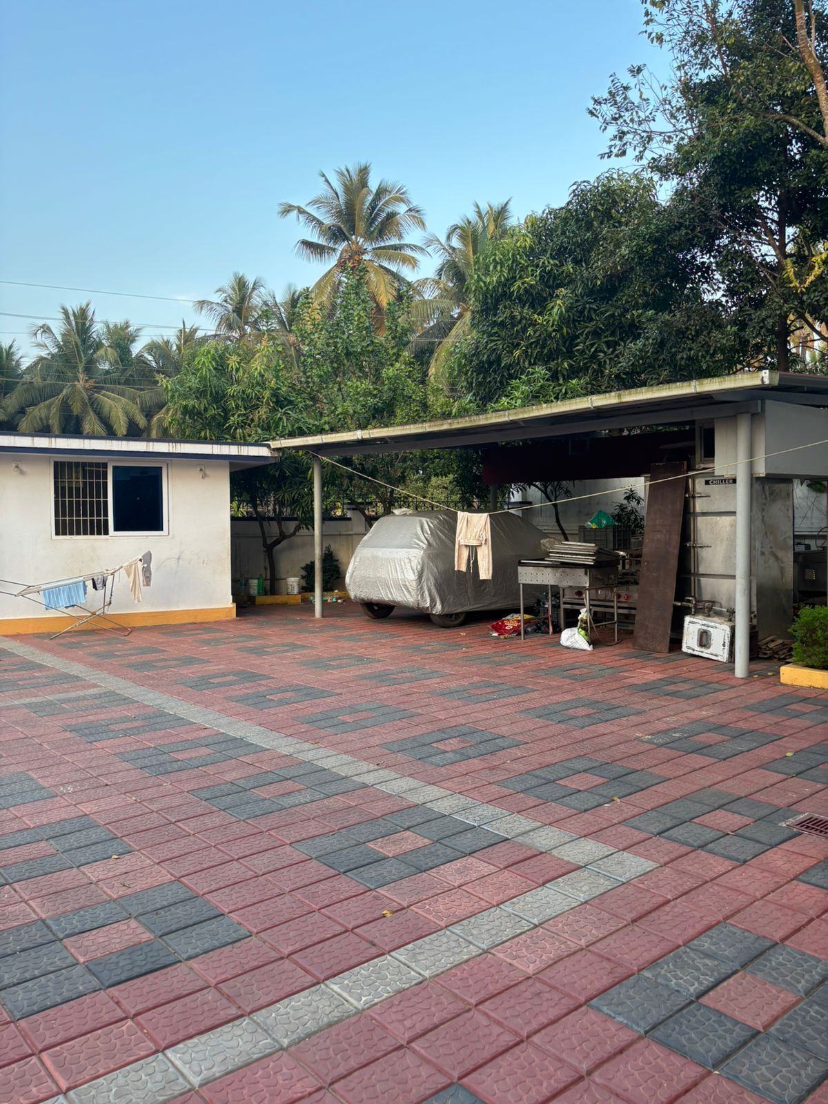 A covered outdoor area with a tiled floor, a covered grill, and a small building with a window.
