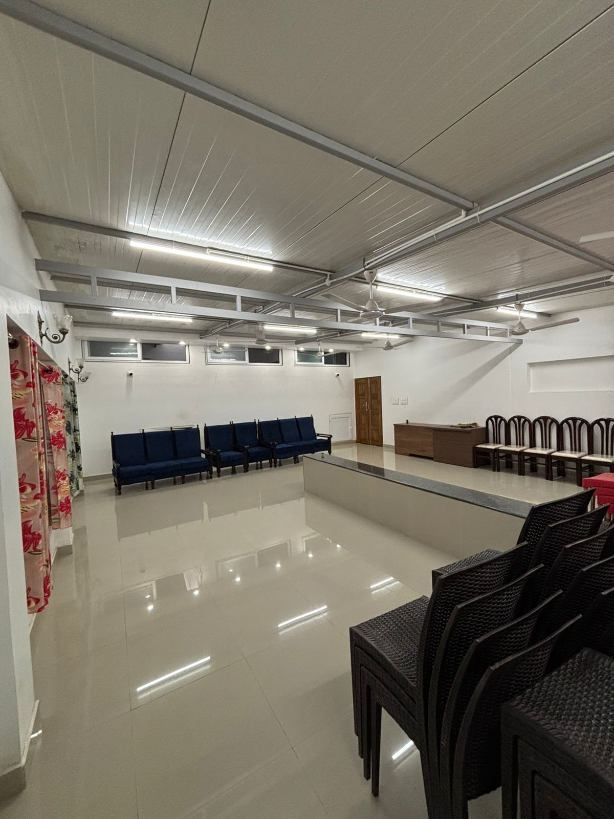 A spacious indoor area with a long row of blue chairs, a reception desk, and a tiled floor.