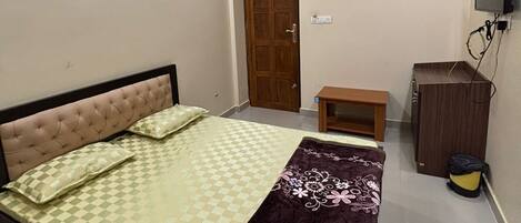 A bedroom with a bed, a ceiling fan, a wooden door, a small table, a TV, and a bag.