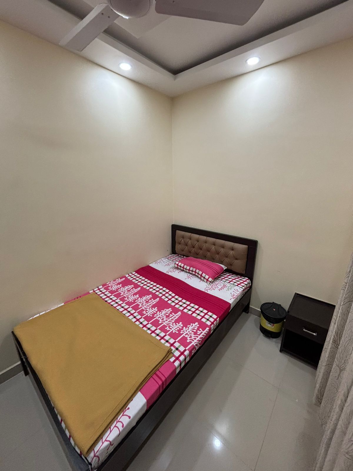 Ein Schlafzimmer mit Bett, Nachttisch, Mülleimer und Deckenleuchte.
