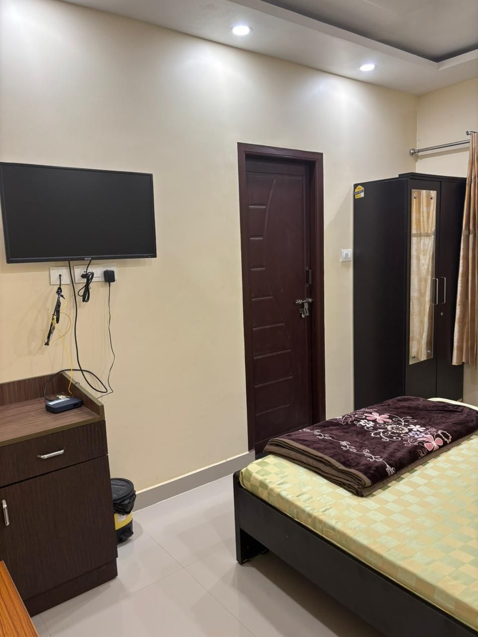 Ein Schlafzimmer mit Bett, Kleiderschrank, Schreibtisch mit Computer und einem an der Wand befestigten Fernseher.