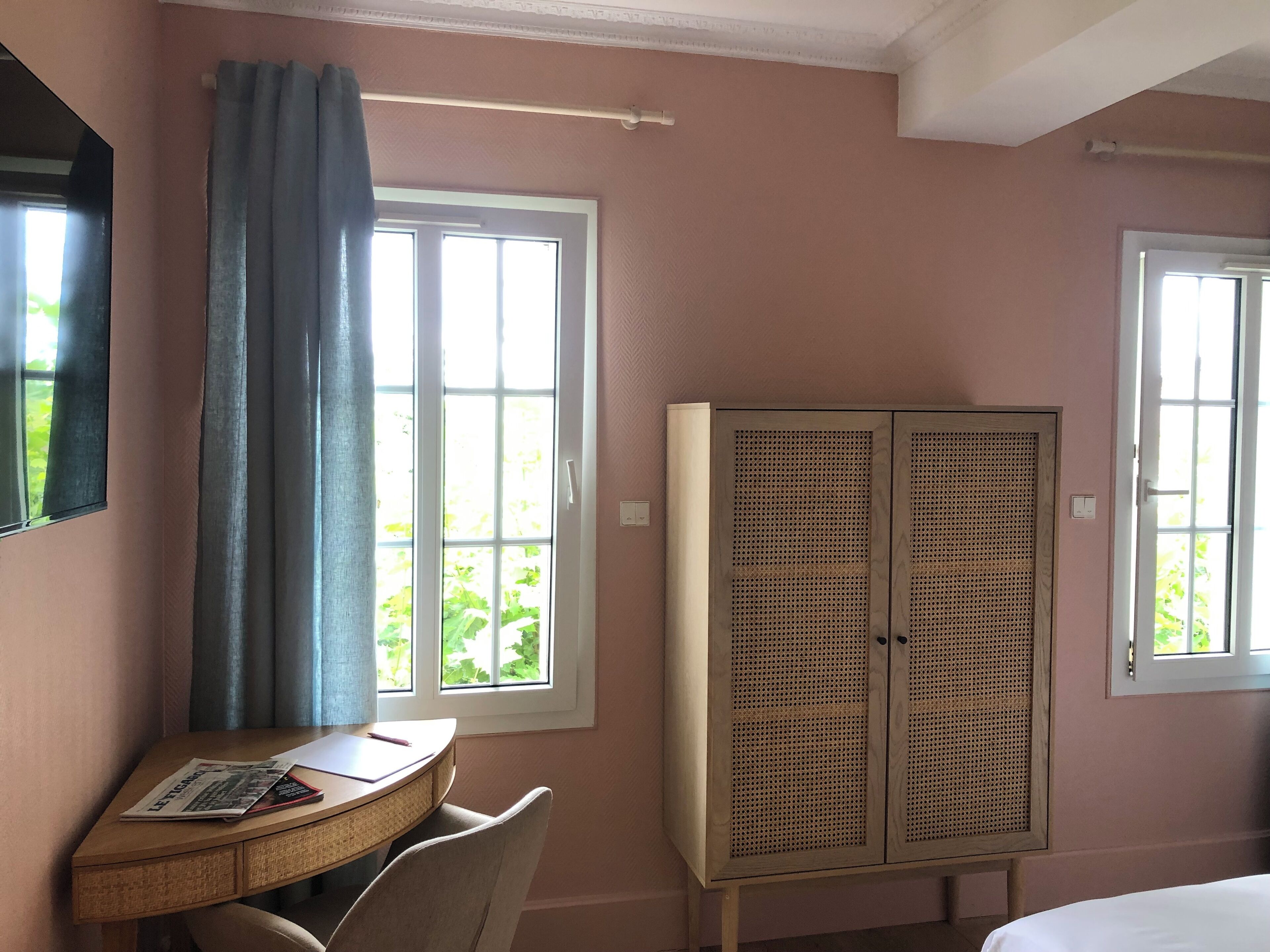 A room with a desk, chair, two windows with curtains, and a wardrobe.