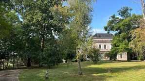 Ein historisches Gebäude mit einer symmetrischen Fassade, umgeben von einem gepflegten Rasen und alten Bäumen.